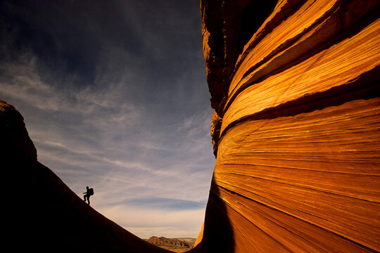 A hiker climbs a ridgeline at "The Wave" sandstone formation in the Paria-Vermillion Cliffs Wilderness, Arizona.