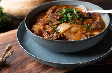 Homemade beef stew with cabbage and vegetables. Served in a grey bowl with spoon on dark wooden and rustic table background