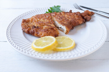 Fresh fried breaded chicken schnitzel on a white plate isolated on white background with lemon and parsley