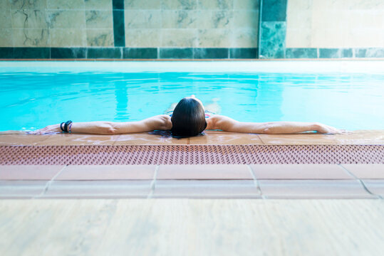 Bikini woman lying relaxing in spa pool on the edge of pool enjoying the blue water