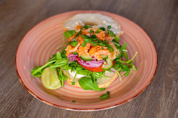 Closeup plate with delicious salmon burger isolated on wooden table background. Serving of healthy sandwich for breakfast. European kitchen, balanced nutrition, restaurant dish, meal