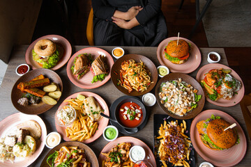 Top view photo of woman sitting at table full of delicious food in plates. Fries, soup, salad, burgers, sauces on festive dinner. Food, many dishes, menu of restaurant, beautiful serving food