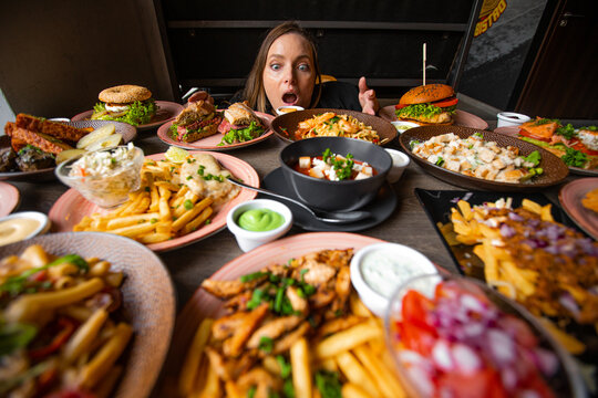 Hungry woman stare on table full of delicious food in plates with open mouth. Fries, soup, salad, burgers, sauces on festive dinner. Food, many dishes, menu of restaurant, beautiful serving food
