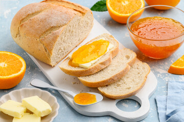 Bread with butter and orange jam on a white board. Tasty breakfast. Orange confiture. Selective focus.