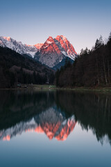 Leuchtender Berg zum Sonnenaufgang mit Schnee an See mit Spiegelung.