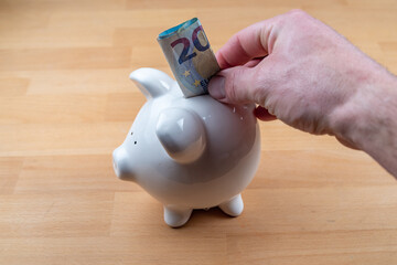 Hand puts 20 euro bill in piggy bank