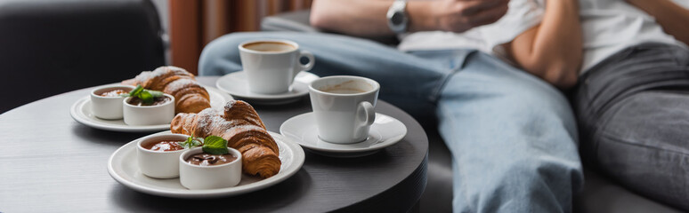 tasty croissants with jam and chocolate paste near coffee cups and cropped couple on blurred...