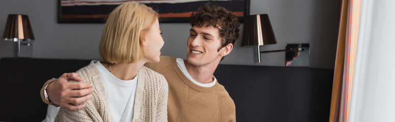 smiling brunette man hugging blonde girlfriend in hotel room, banner.