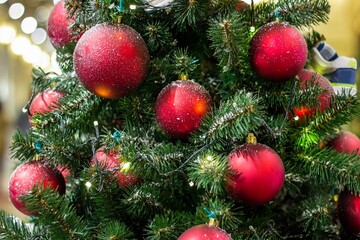 Christmas tree background and Christmas decorations in the mall. Colorful red balls and ribbons on green fir. New Year theme