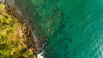 Aerial view of turquoise water of Pacific Ocean, Sri Lanka. A group of surfers are waiting for the waves from above.