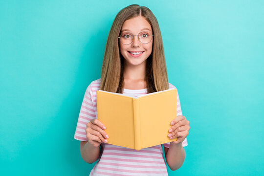 Portrait of cheerful clever girl toothy smile arms hold book isolated on aquamarine color background