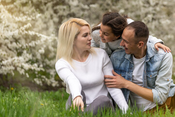 Obraz premium Happy family outdoors spending time together. Father, mother and daughter are having fun on a green floral grass.