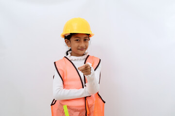 Asian little girl in the construction helmet as an engineer standing while pointing at the camera. Isolated on white with copyspace