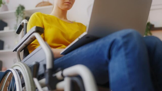 Close-up of young woman wheelchair user working on laptop in home office