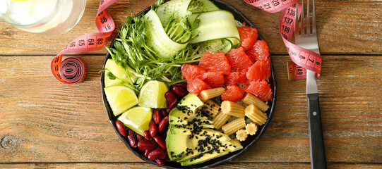 Plate with delicious fresh salad and measuring tape on wooden table. Diet concept