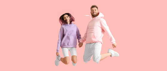 Cool jumping young couple in hoodies on pink background