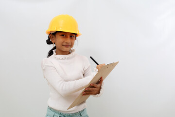 Happy Asian little girl in the construction helmet as an engineer standing while writing something. Isolated on white