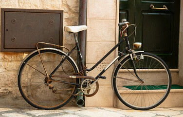 Fototapeta na wymiar A vintage bicycle, cover with rust secure by the downspout near a home entrance in Italy, Bari. Nice old bike used by locals. Retro bike near a door.