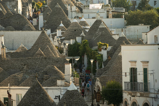 A street in Alberobello going up between the rocky houses with tourist all over the see the Unesco town. Nice sunset over rocky rooftops.