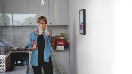 medium full shot of a young woman holding a screwdriver and showing thumb up in the kitchen, repair...
