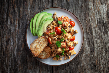 A plate on a rustic wooden table with plant based, vegan scrambled tofu, avocado and light fried bread served on a ceramic plate