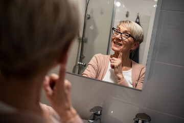 Confident senior woman looking at her reflection in the mirror and talk to himself. Trying to rise self-esteem and motivate himself.