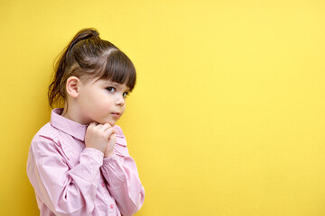 girl child thoughtfully planning an idea, thinking looking suspiciously, caucasian child isolated on yellow background, portrait
