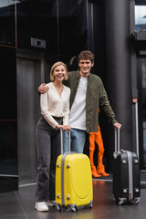 Fototapeta na wymiar young man with blonde girlfriend standing with suitcases and laughing in lobby of hotel.