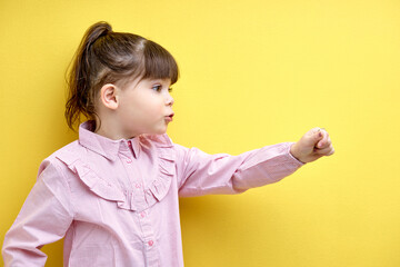 Side view portrait of child girl looking at side and speaking, points hand forward, funny and...