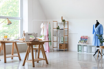 Interior of light atelier with tailor's workplace, clothes and mannequin