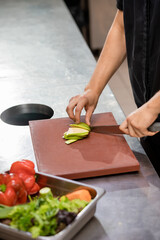 Professional chef in uniform preparing fresh vegetables on cutting board in restaurant kitchen. Culinary concept