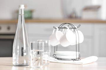 Bottle of water, glasses and cups on table in kitchen