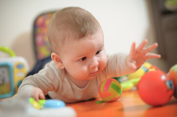 Fototapeta na wymiar Baby plays with toys. Close-up view of cute baby boy lies on its stomach with an outstretched hand holding a toy and learns about the world around him