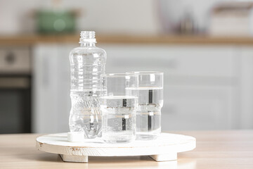 Stand with bottle of water and glasses on table in kitchen