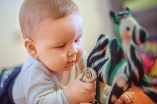 Baby plays with toys. Close-up view of cute baby boy lies on its stomach with an outstretched hand holding a toy and learns about the world around him
