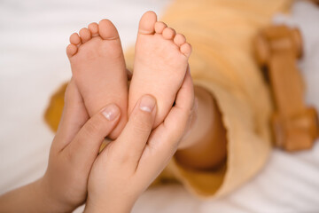 Mother massaging her baby's feet in bedroom, closeup
