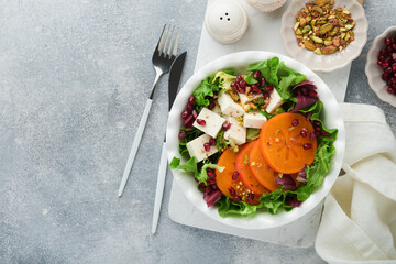 Salad. Fresh green salad with feta cheese, persimmon, pomegranate and pistachio on white plate. Idea for healthy delicious winter Christmas salad. Healthy balanced eating. Top view.