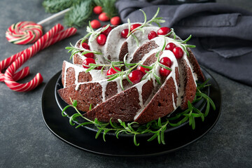Christmas chocolate bundt cake. Traditional Christmas fruit cake with white glaze, cranberries and rosemary on dark backgroundChristmas decoration. Winter baking at Xmas or New Year. Copy space.