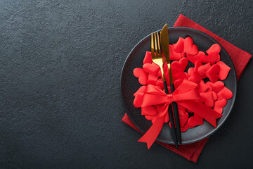 Valentines day romantic table setting. Empty or closeup of a dinner black plate, knife, fork and decorative silk hearts on black background. Holiday concept. Copy space for inscriptions. - obrazy, fototapety, plakaty
