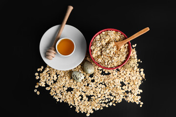 Bowl of raw oatmeal, honey and quail eggs on dark background