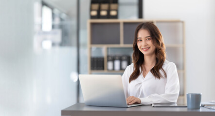 Charming Asian woman working at the office using a laptop Looking at the camera.