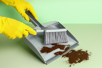 Woman in rubber gloves sweeping coffee with dustpan and brush on color background