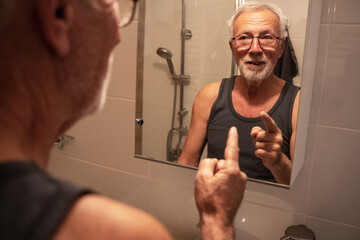 Confident senior man looking at his reflection in the mirror and talk to himself. Trying to rise self-esteem and encourages himself.