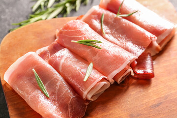 Wooden board with rolled slices of delicious ham, closeup