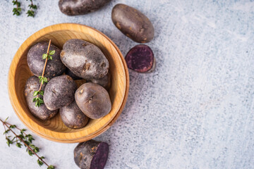 Wooden bowl of raw purple potatoes and thyme on light background