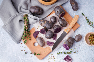 Wooden board with raw purple potatoes, knife and thyme on light background