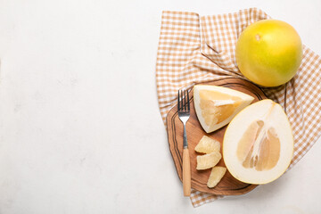 Wooden board with fork, pomelo fruit and slices on light background