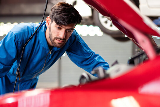 Caucasian auto mechanic young man checking and repairing car radiator bonnet in automotive condition in garage at auto repair shop, motor technician working after vehicle service maintenance concept