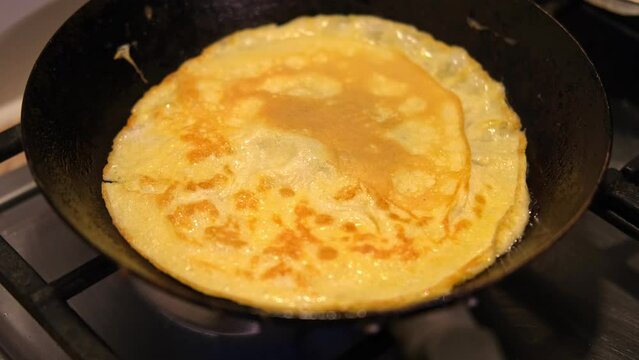Chef cooking tasty scrambled eggs on kitchen. Homemade Omelette. Fried eggs in a black skillet. Top view. Golden sauteed eggs on the frying pan. Modern cuisine. Preparing breakfast. Cooking at home.