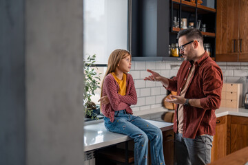Upset father having a serious conversation with his young stubborn daughter, gesturing with hands, arguing. Girl is sitting with the arms crossed and looking at him.